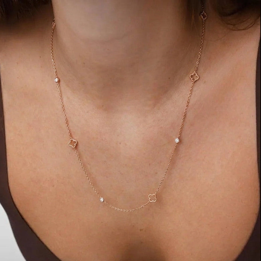 A close-up of a model wearing a delicate rose gold chain necklace with small diamond-shaped and pearl accents.