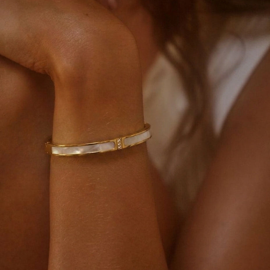 A close-up of a gold bangle bracelet with white inlay, worn on a person's wrist.